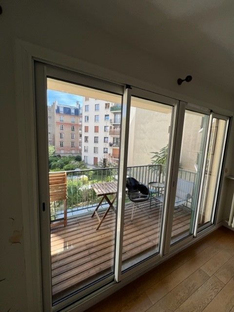 Balcon d'appartement avec terrasse en bois, chaise noire et vue sur les immeubles voisins à travers les portes vitrées