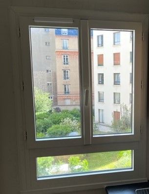 Vue à travers une fenêtre à cadre blanc sur des immeubles d'appartements et une cour extérieure verdoyante