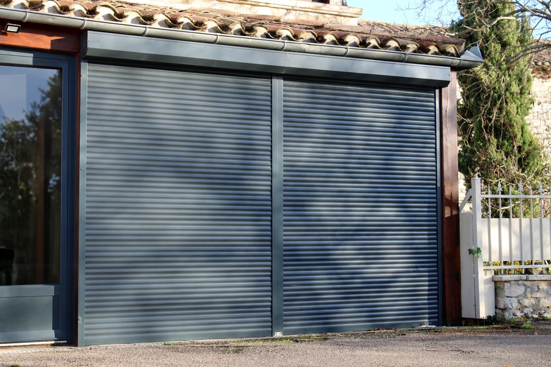 Une porte de garage sectionnelle gris anthracite fermée, installée dans un bâtiment au toit de tuiles.