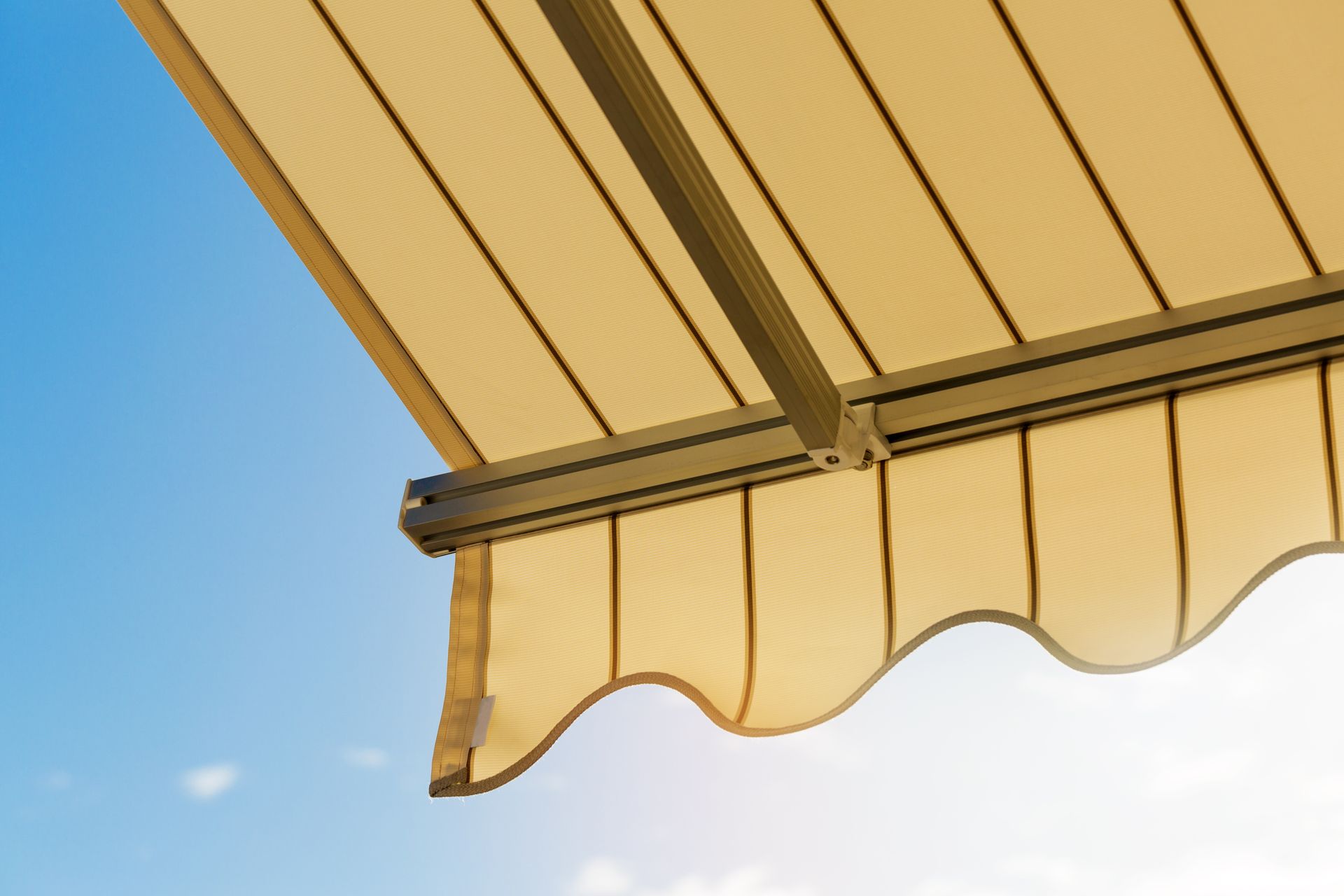Un store banne beige rétractable à bord festonné se déploie sur un ciel bleu limpide.