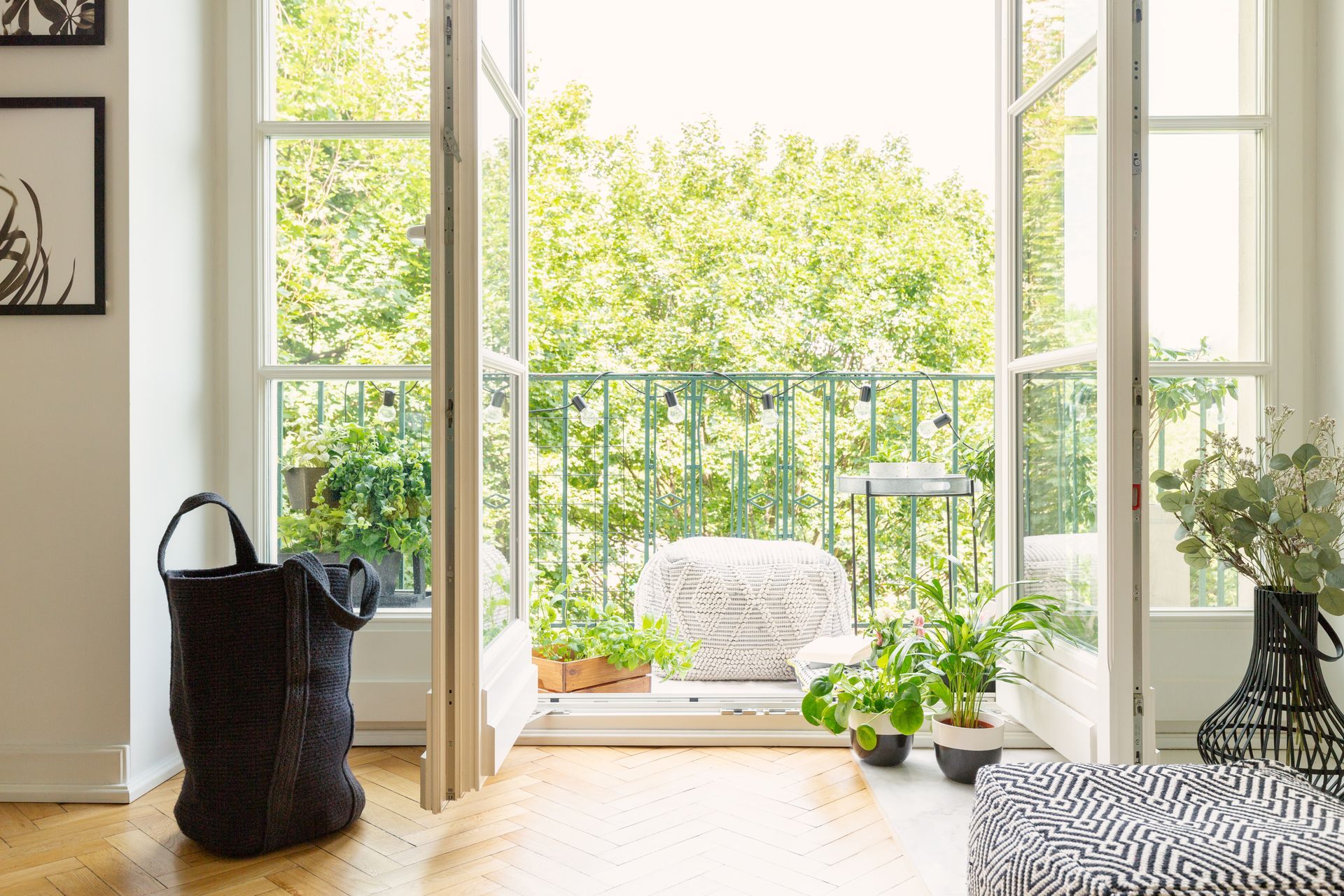 Une porte-fenêtre baignée de soleil s'ouvre sur un balcon agrémenté de plantes.