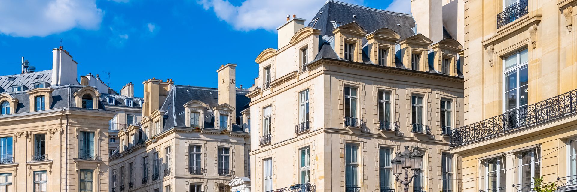Immeubles parisiens classiques en pierre calcaire aux détails architecturaux complexes, sous un ciel d'un bleu éclatant.