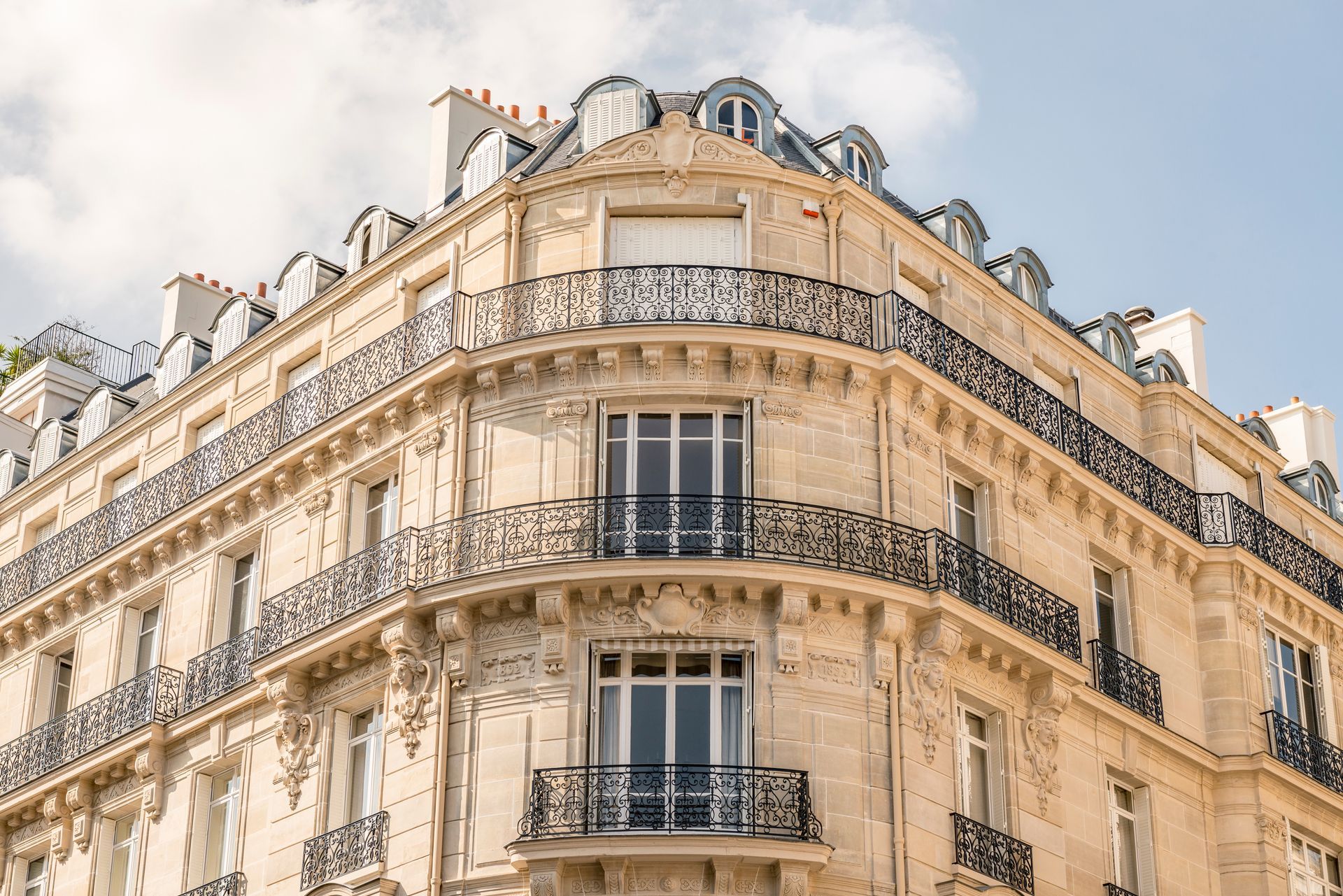 Vue en contre-plongée d'un immeuble haussmannien beige et orné, à Paris, avec des balcons en fer forgé.