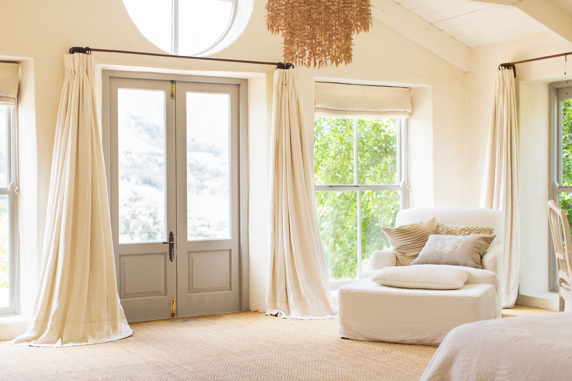 Cette pièce baignée de soleil présente une décoration neutre, des rideaux couleur crème, une paire de portes-fenêtres.