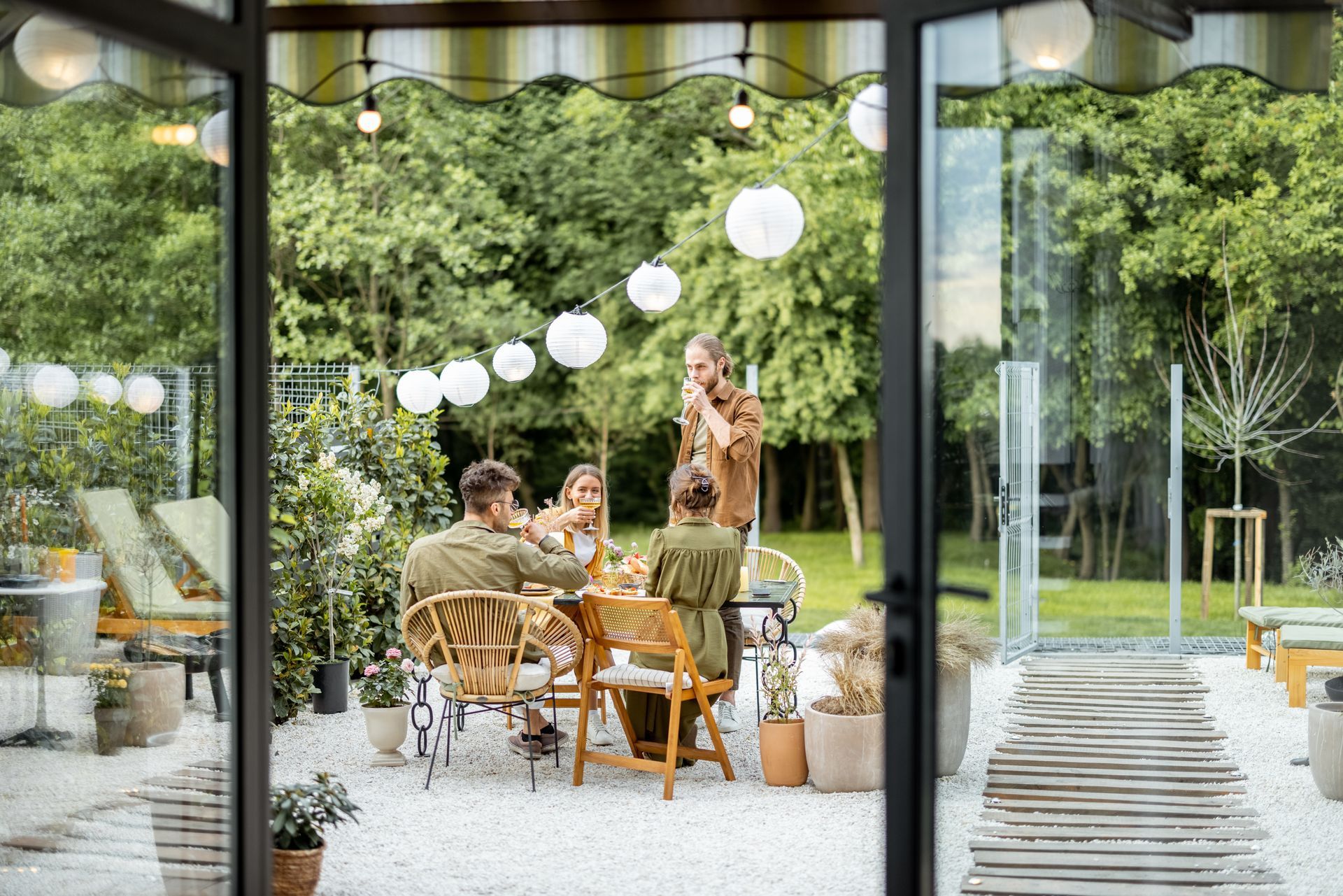 Un groupe de personnes dînant en plein air sur une terrasse en gravier sous des guirlandes lumineuses.