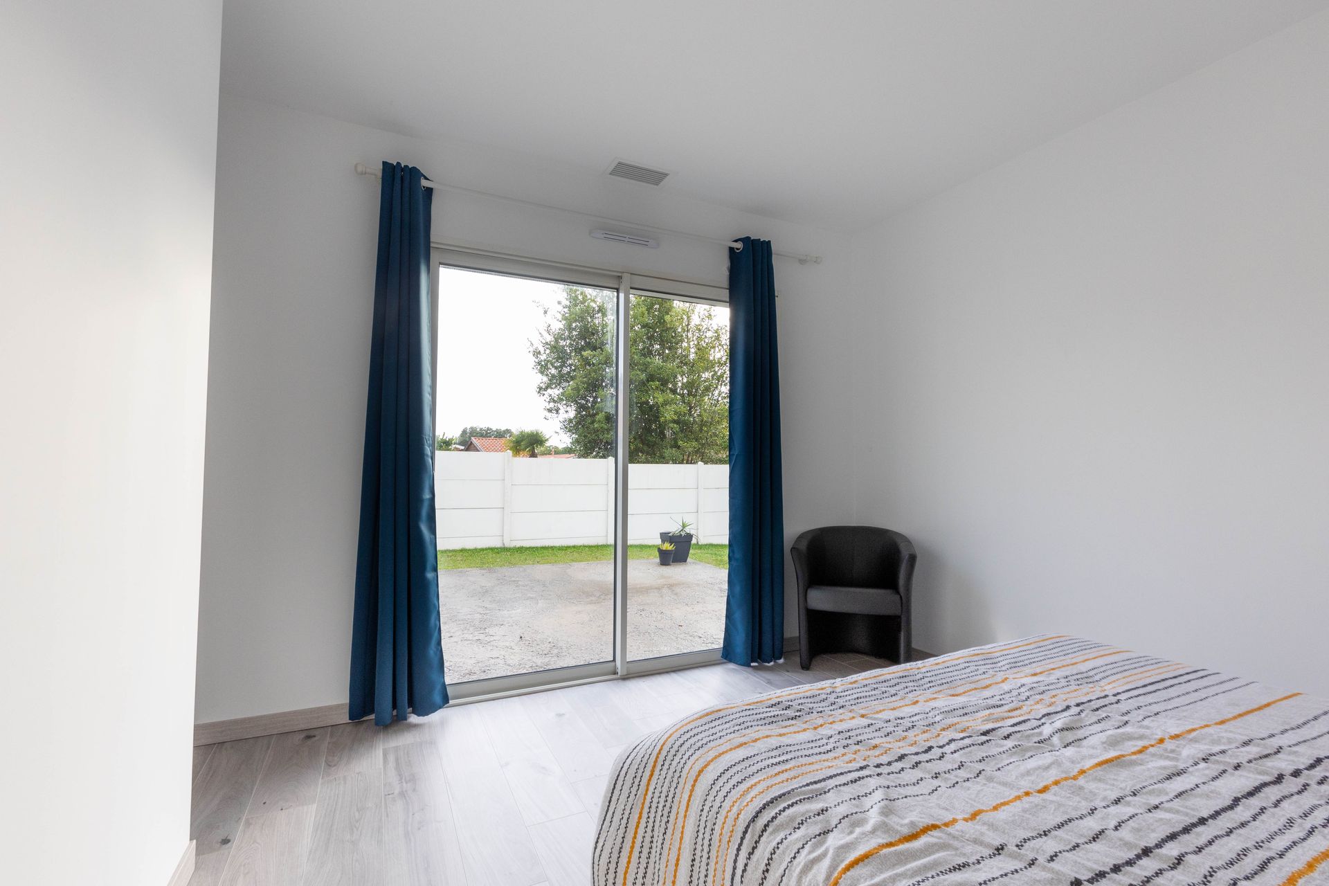 Une chambre minimaliste avec des murs blancs, un lit recouvert d'une couette à motifs, des rideaux bleu foncé.