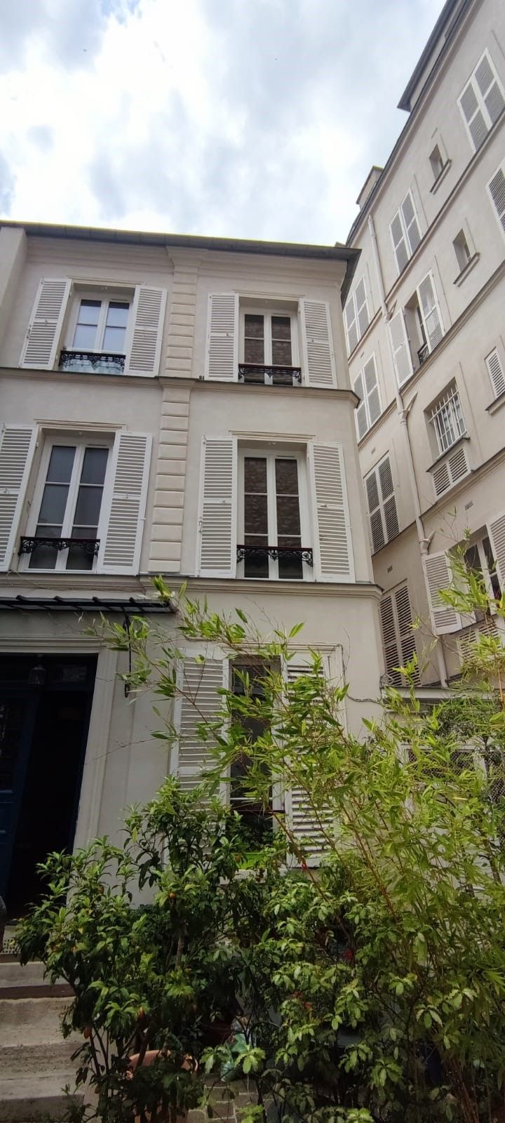 Vue sur la cour intérieure d'immeubles d'appartements couleur crème aux fenêtres à volets et à la végétation en contrebas.