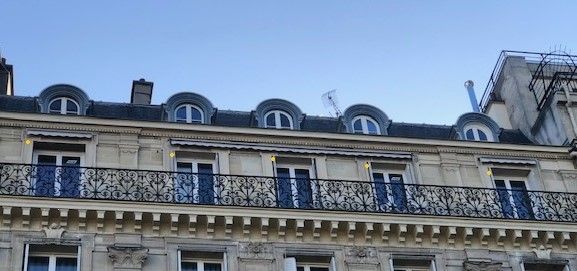 Façade d'immeuble ornée de style parisien avec auvents et balcons bleus sous un ciel gris