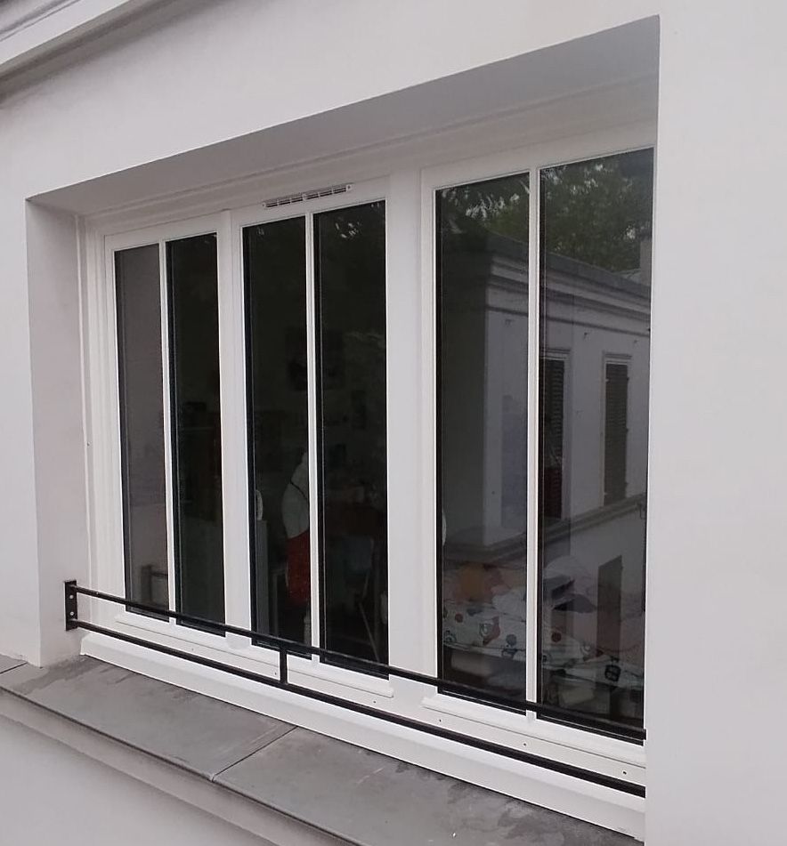 Mur extérieur blanc avec une grande baie vitrée coulissante et une petite rambarde de balcon en dessous.