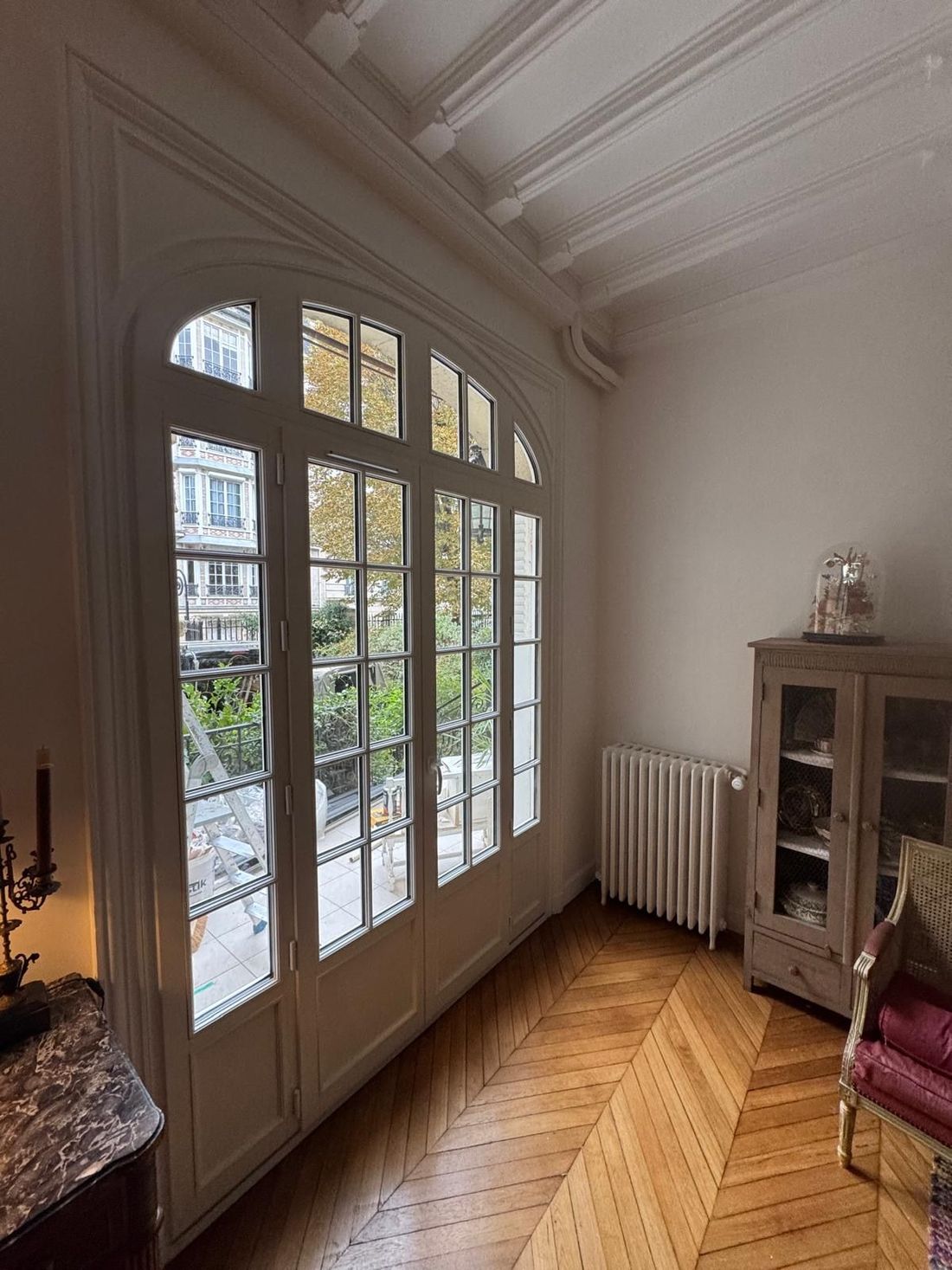 Une porte-fenêtre blanche à plusieurs panneaux, au sommet incurvé, placée dans une arche en pierre.