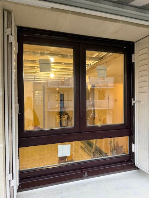 Fenêtre à cadre foncé avec éclairage intérieur chaleureux et stores, vue depuis un petit balcon ou une terrasse.