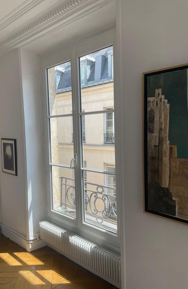 Une fenêtre à encadrement blanc et volets bleu foncé sur un mur en stuc, avec une rambarde décorative en métal noir.