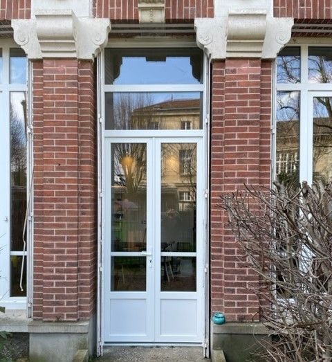 Entrée d'un bâtiment en briques avec double porte blanche et hautes fenêtres