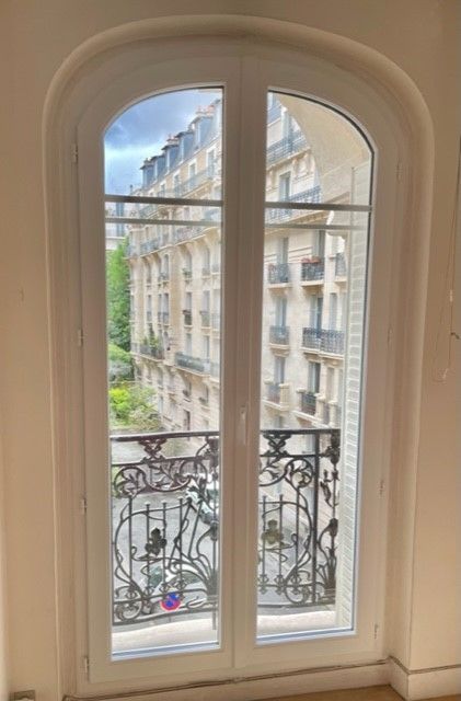 Des portes-fenêtres ouvertes encadrent une vue sur une rue parisienne avec des balustrades de balcon ouvragées.