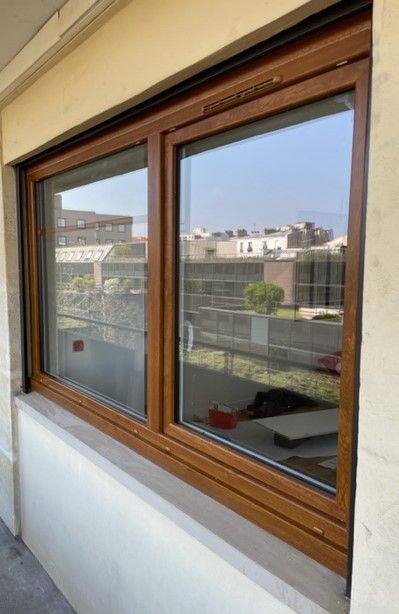 Fenêtre coulissante à cadre en bois reflétant les bâtiments environnants et vue sur le balcon