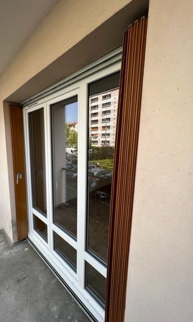 Porte coulissante en verre avec cadre blanc et revêtement brun sur l'extérieur d'un bâtiment.