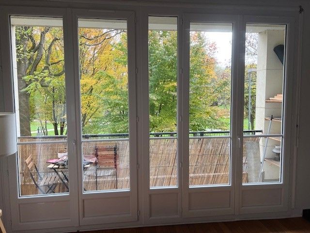 Les fenêtres du salon s'ouvrent sur un balcon bordé d'arbres aux couleurs d'automne.
