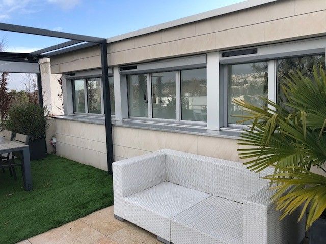 Patio avec canapé en osier blanc à côté d'une maison moderne, pelouse verte et palmier sous une pergola couverte