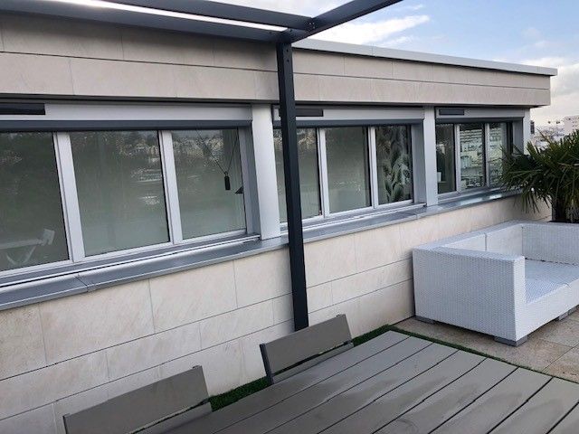 Patio moderne avec terrasse en bois grise, grandes fenêtres et sièges d'extérieur blancs à côté d'un bâtiment