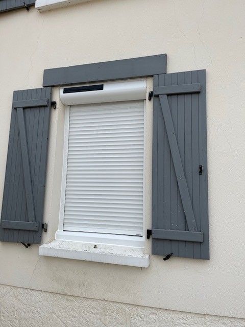 Fenêtre à volets blancs avec volets en bois gris sur un mur extérieur beige
