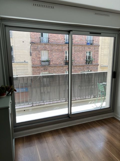Pièce vide avec parquet et grandes portes coulissantes en verre donnant sur un immeuble en briques et un balcon.