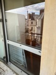Fenêtre d'appartement avec climatiseur de fenêtre, reflétant les bâtiments voisins à l'extérieur.