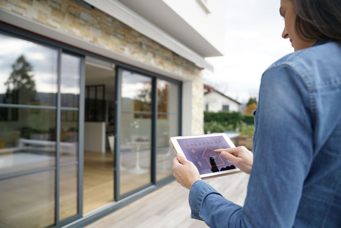 Une personne vêtue d'une chemise en jean utilise une tablette pour contrôler les fonctionnalités intelligentes de sa maison.