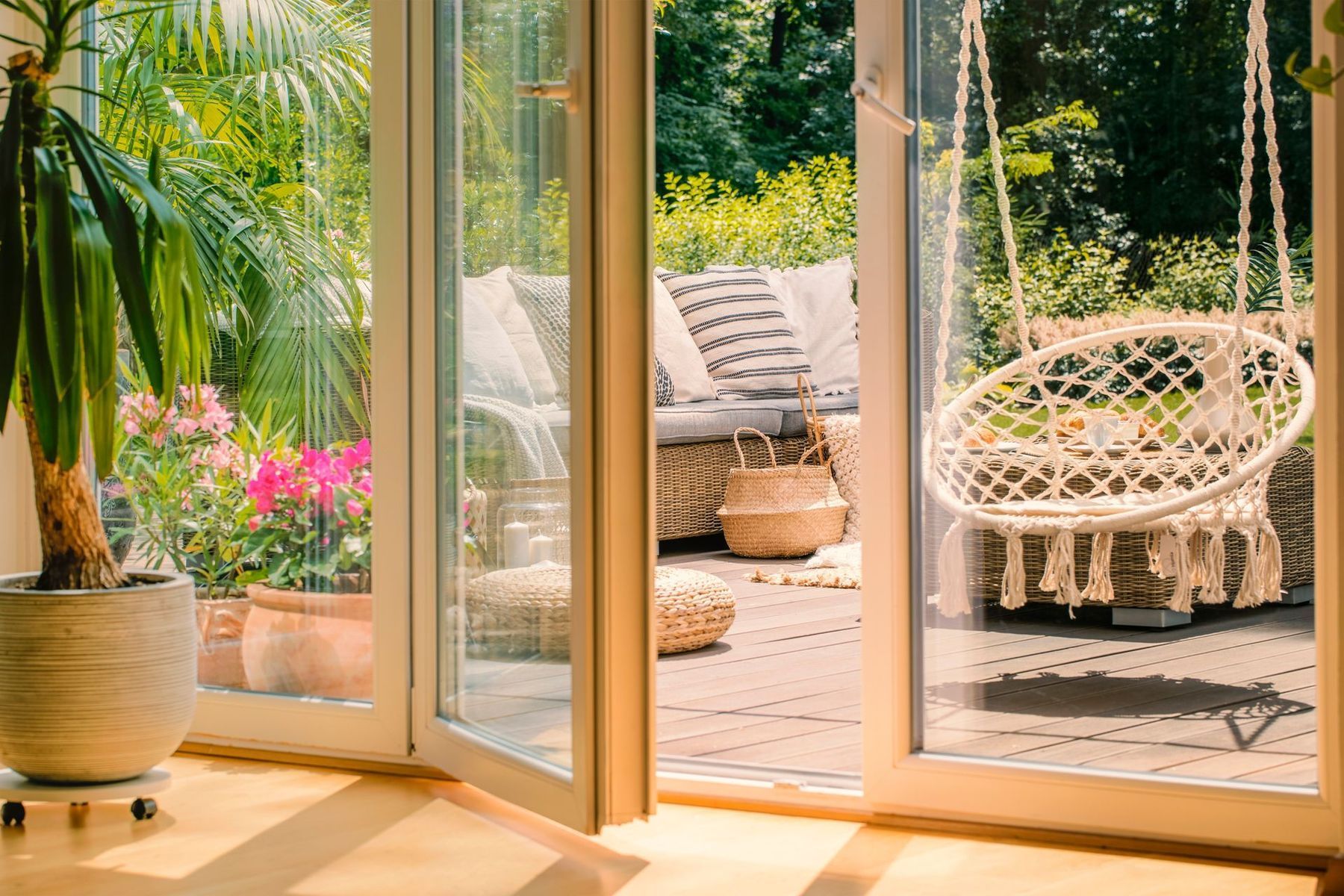 Vue d'une terrasse extérieure ensoleillée avec un fauteuil suspendu et un canapé en osier.