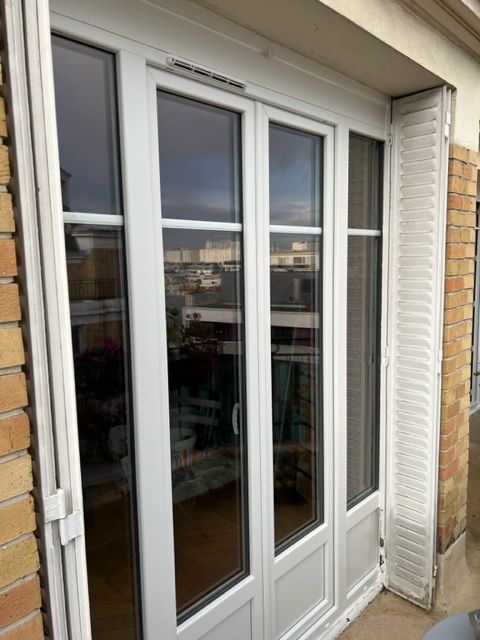 Porte-fenêtre en verre blanc avec fenêtres latérales étroites sur un mur extérieur en briques.