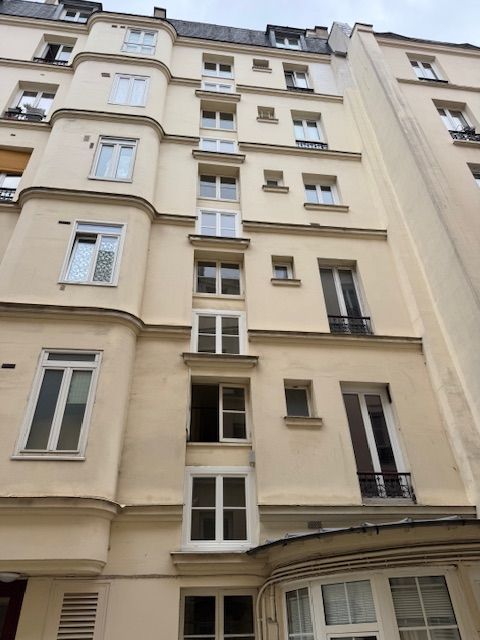 Façade d'un immeuble d'appartements beige de grande hauteur, avec de nombreuses fenêtres et balcons, vue d'en bas.