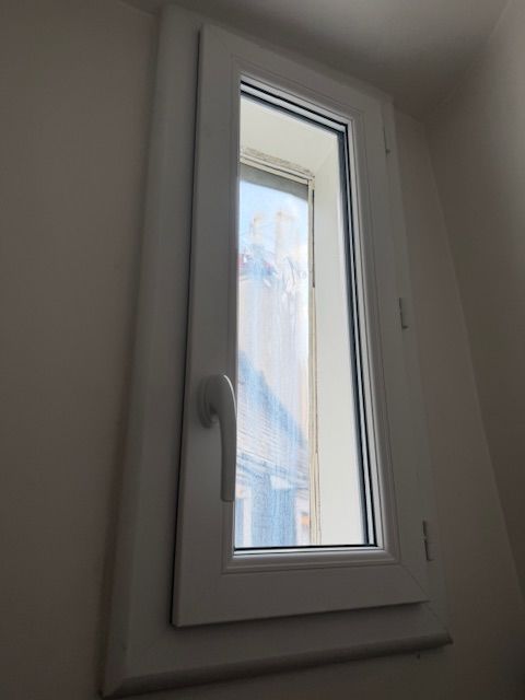 Fenêtre oscillo-battante blanche à verre dépoli dans un mur clair.