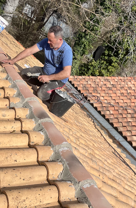 Ouvrier à genoux sur un toit qui cimente les tuiles de faîtage
