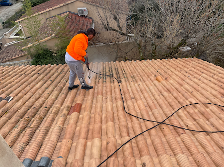 Homme avec un haut orange qui enlèeve la mousse de toit avec un karcher
