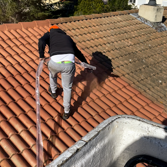 Ouvrier appliquant une peinture hydrofuge sur un toit dont la moitié est faite