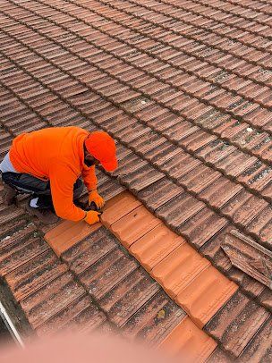 Homme en veste et casquette orange changeant des tuiles sur un toit