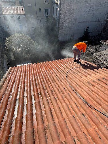 ouvrier en bord de toit nettoyant les tuiles au karcher