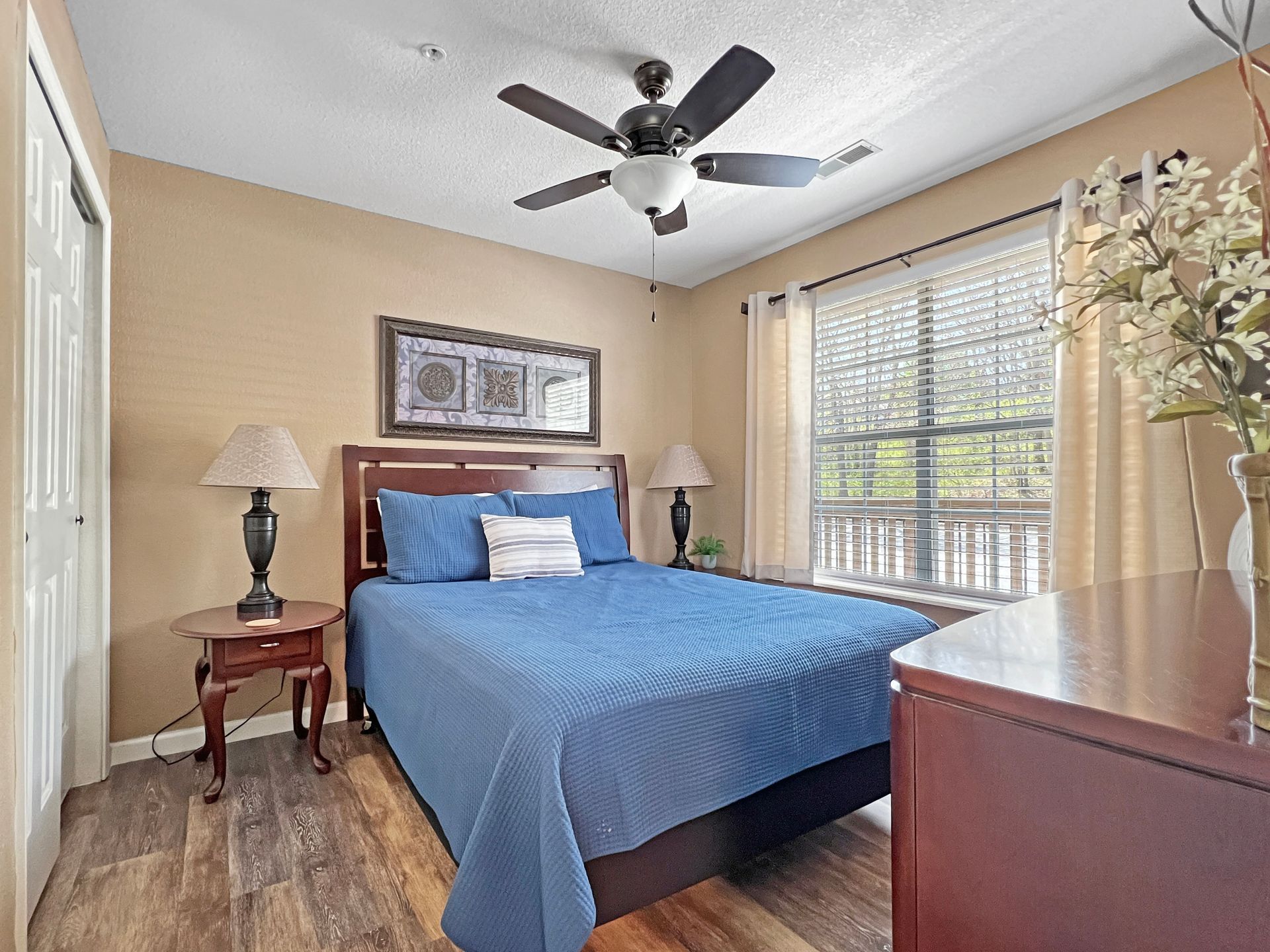 A bedroom with a bed , dresser , lamps and a ceiling fan.
