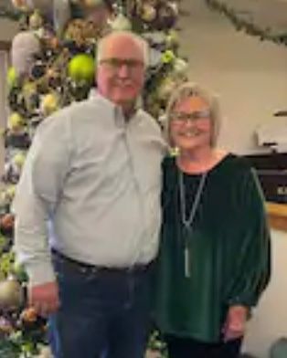 A man and a woman are posing for a picture in front of a christmas tree.