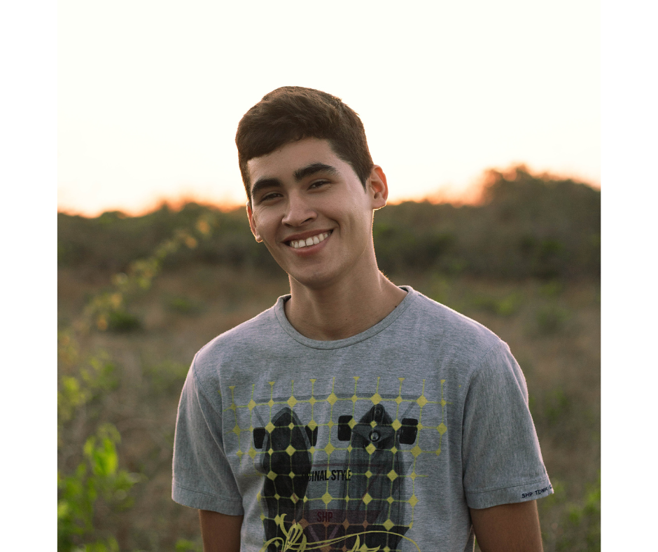 A young man wearing a gray t-shirt is smiling in a field.