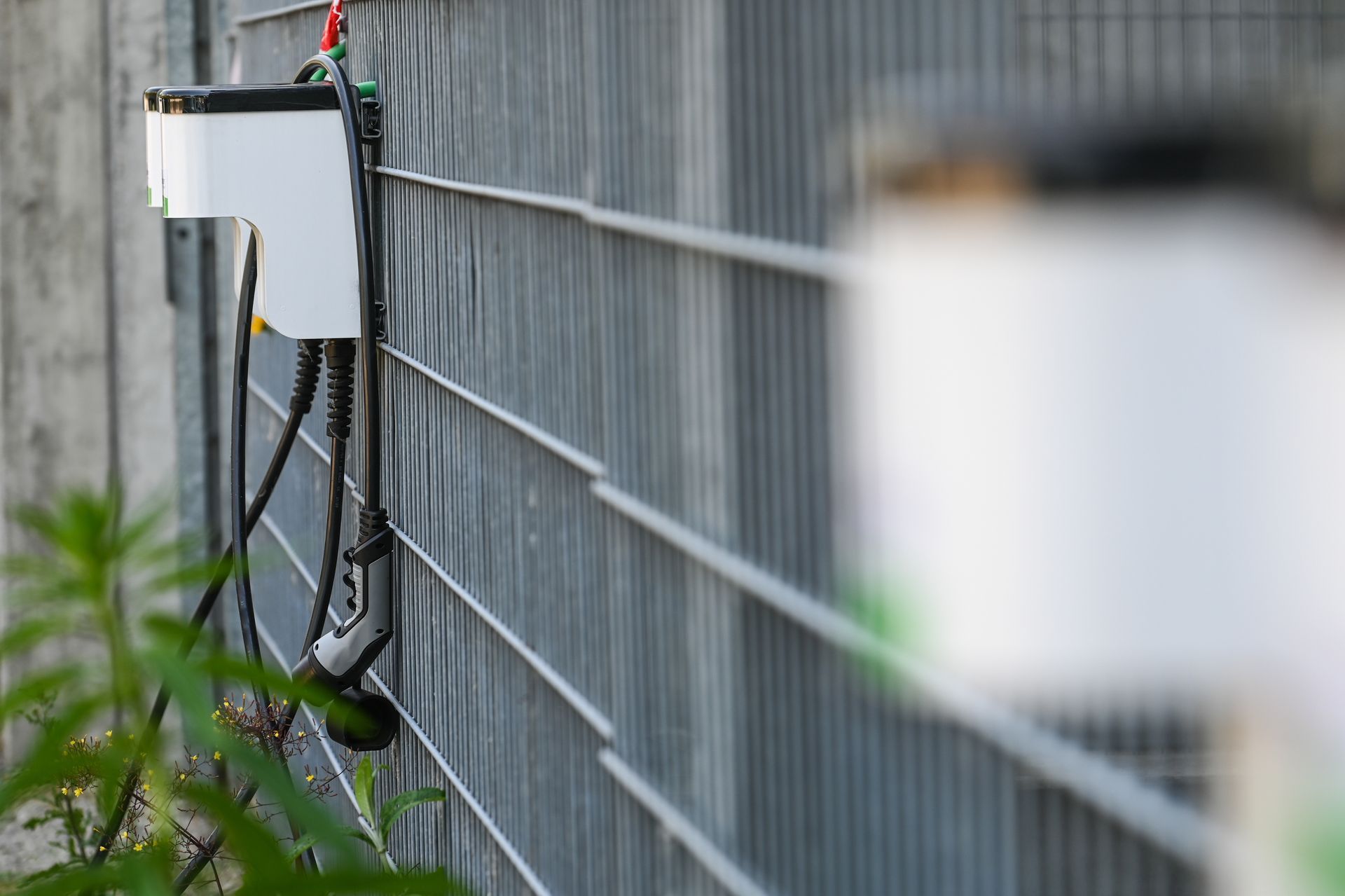 Borne de recharge pour véhicule électrique montée sur une clôture métallique avec câbles de recharge.