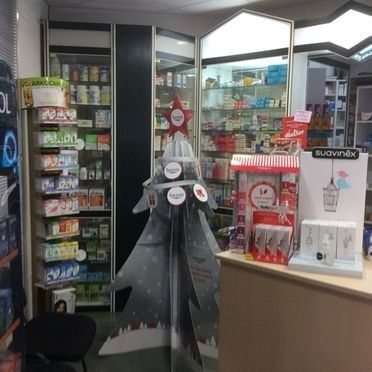 Interior de una farmacia, con estantes llenos de productos y una exhibición con temática navideña.