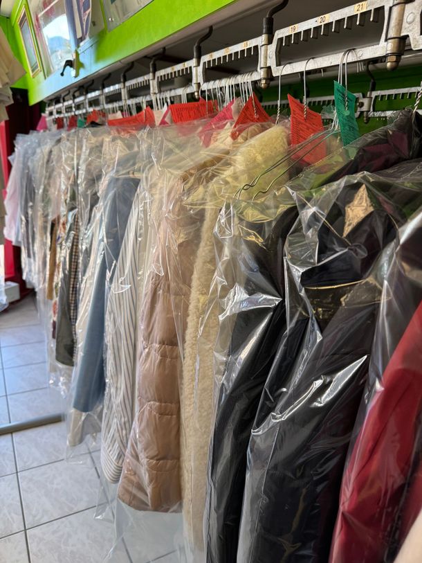 Mäntel in Plastikkleidersäcken, die in verschiedenen Farben an einem Ständer in einer Reinigung hängen.