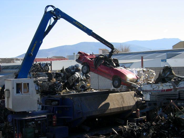 Una grúa levanta un coche rojo y lo mete en un contenedor de basura.