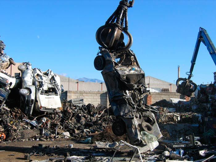 Una grúa está levantando un coche en un depósito de chatarra.