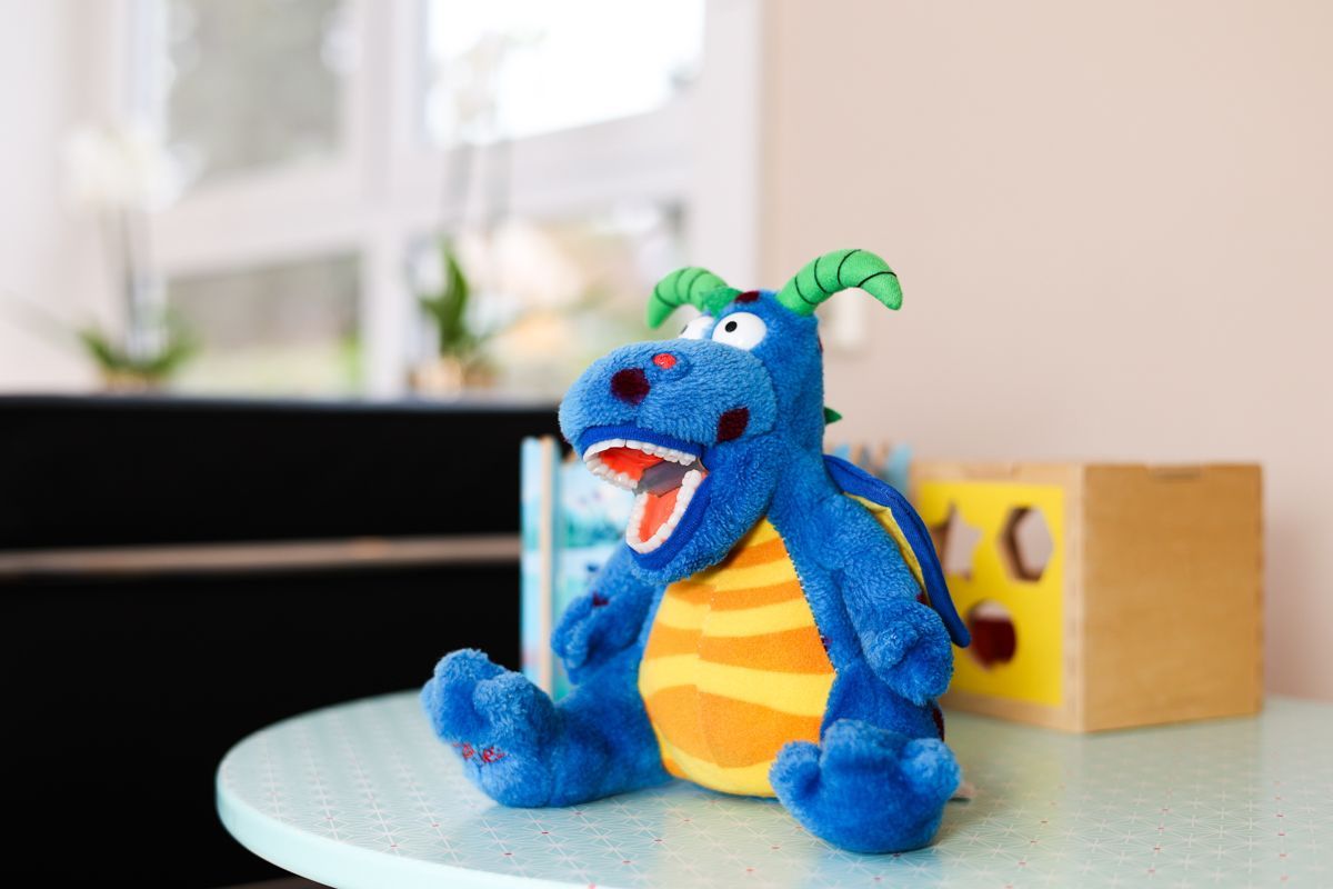 Auf einem Tisch sitzt ein blauer Stoffdrache.