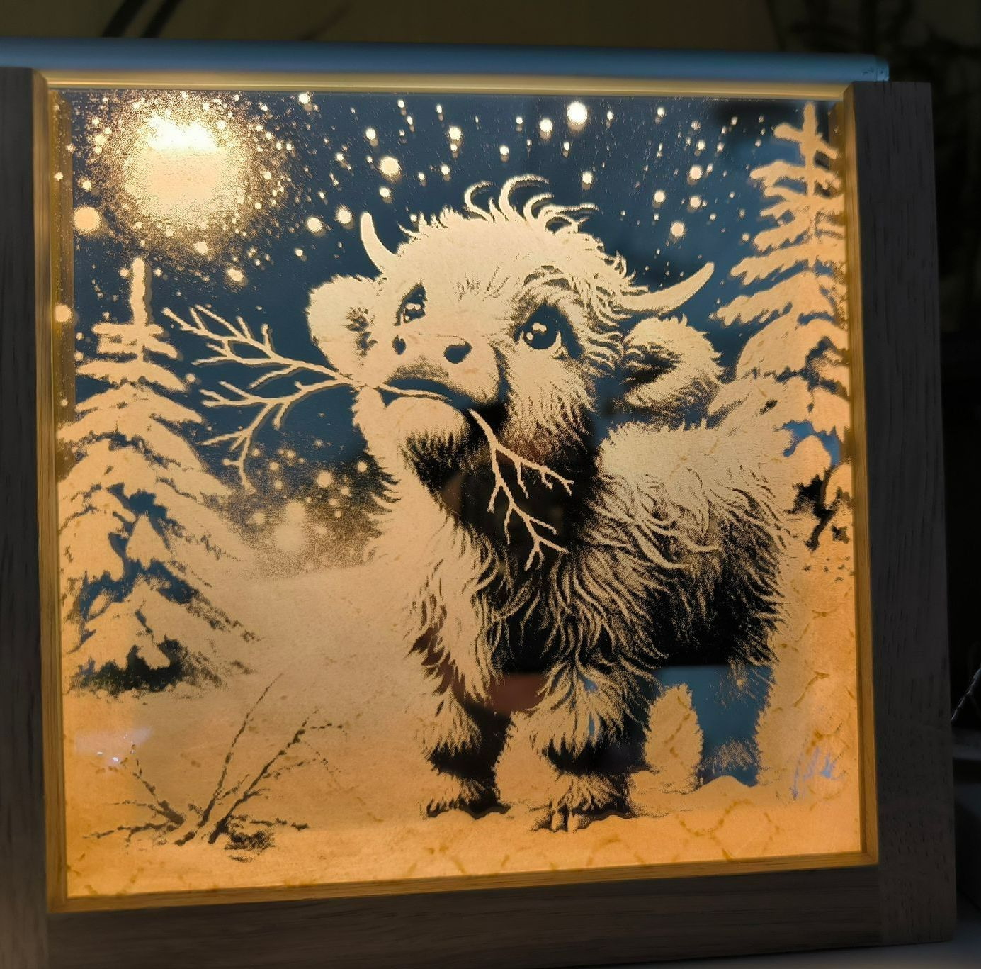 Ein beleuchtetes Bild von einem Baby Hochlandrind im Schnee mit Bäumen im Hintergrund