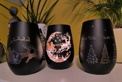 Auf einem Tisch stehen drei schwarze gravierte Gläser mit Weihnachtsmotiven.