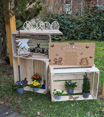 Eine Holzkiste gefüllt mit Topfpflanzen und Osterdekorationen.