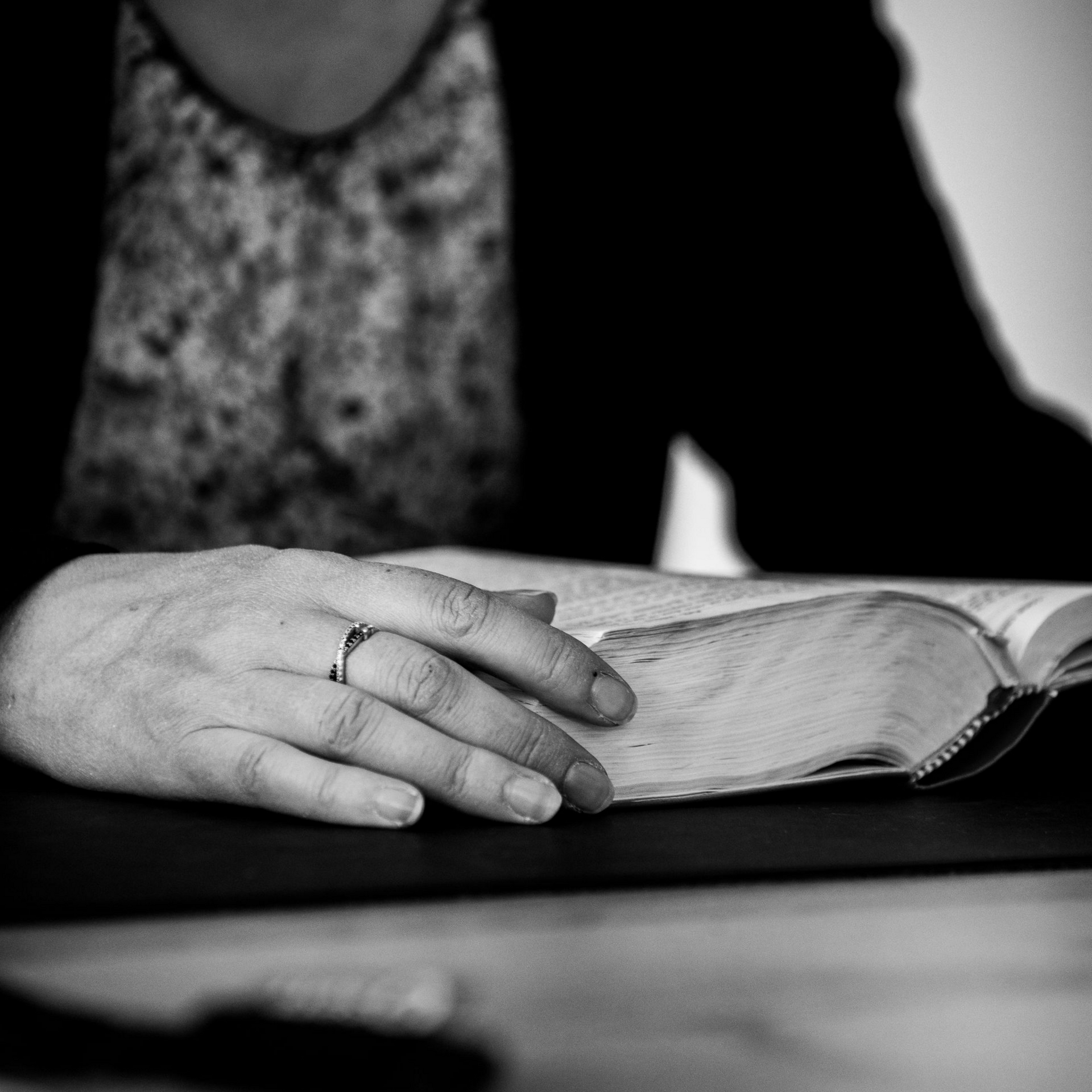 Une main posée sur un livre ouvert, en noir et blanc, sur une table.