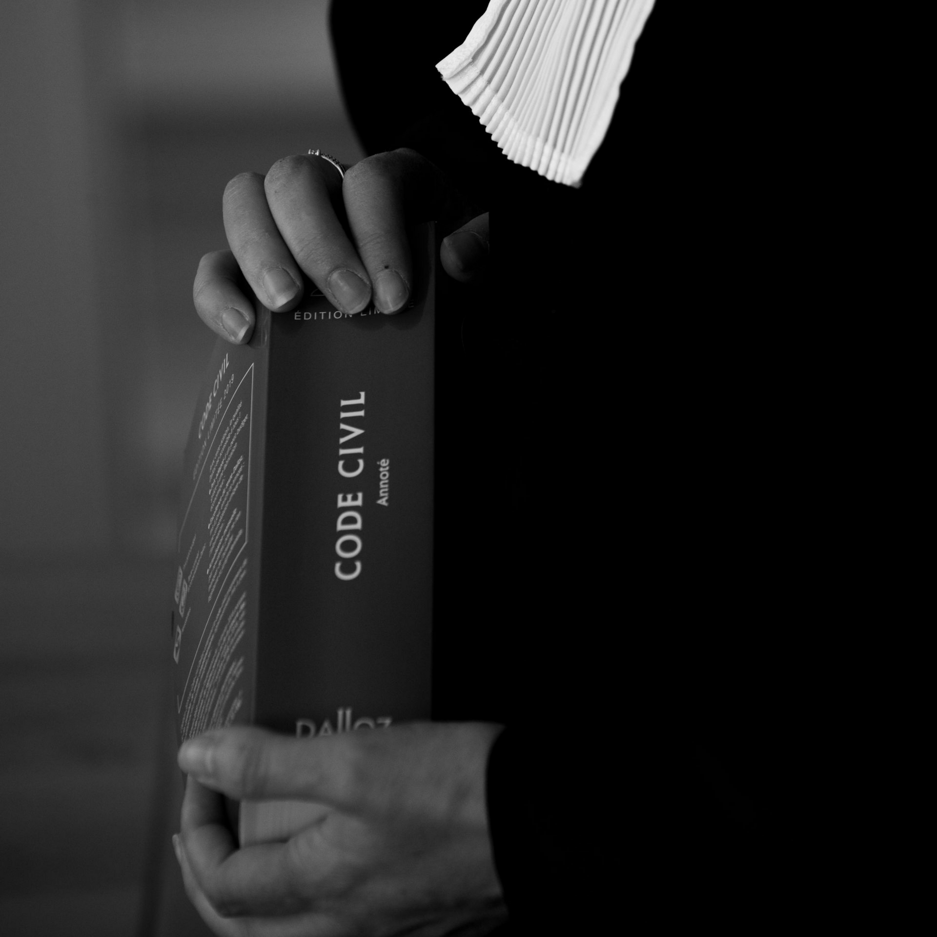 Des mains tenant un livre noir portant l'inscription CODE CIVIL en niveaux de gris.